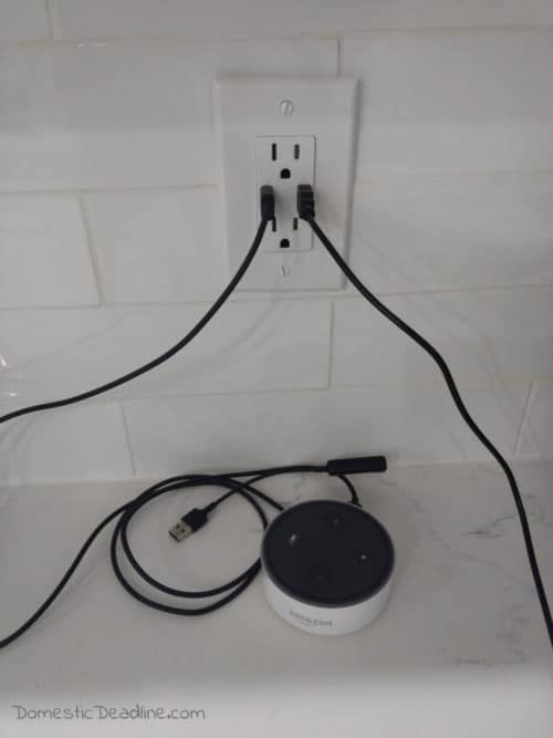 An easy and inexpensive way to hang your Amazon Alexa Dot on the wall near the outlet. This DIY Alexa Dot Holder uses a hose clamp and command hooks. Upcycle Challenge www.domesticdeadline.com