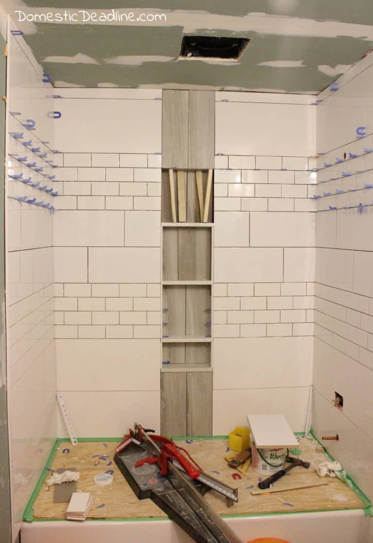 Learn how I create an industrial farmhouse bathroom using classic subway tile, but with a twist! Incorporating storage to reduce bathtub ledge clutter. DomesticDeadline.com