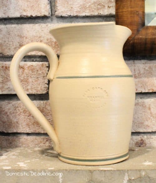 Learn how a few coats of paint can easily transform an old dated ceramic pitcher into a classic farmhouse pitcher full of greenery for mantel decor. DomesticDeadline.com