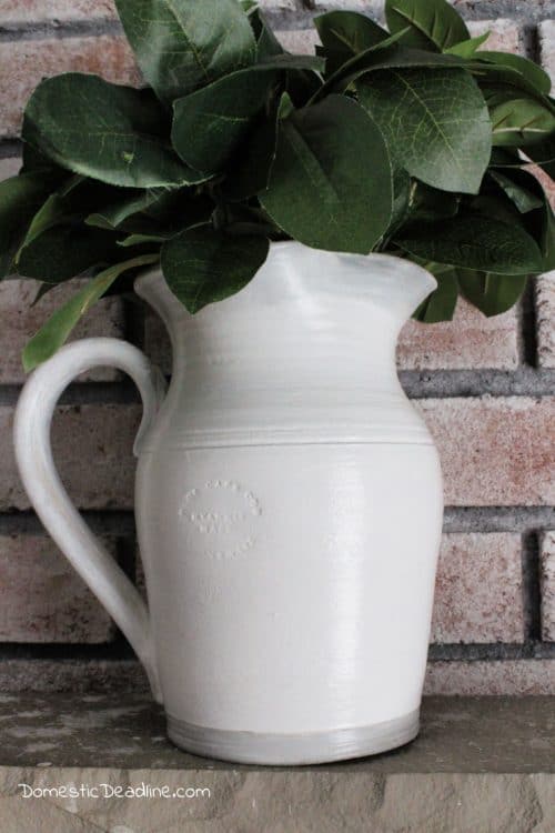 Learn how a few coats of paint can easily transform an old dated ceramic pitcher into a classic farmhouse pitcher full of greenery for mantel decor. DomesticDeadline.com