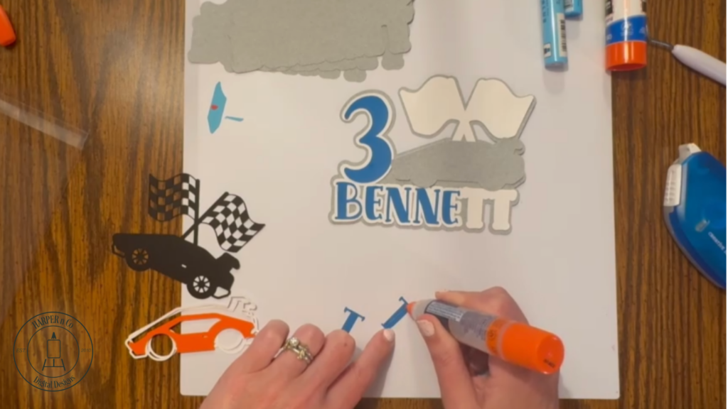 Layering cardstock details onto a cake topper including letters, numbers, and car shapes.