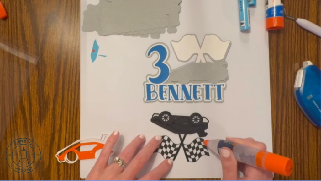 Layering cardstock details onto a cake topper including letters, numbers, and car shapes.