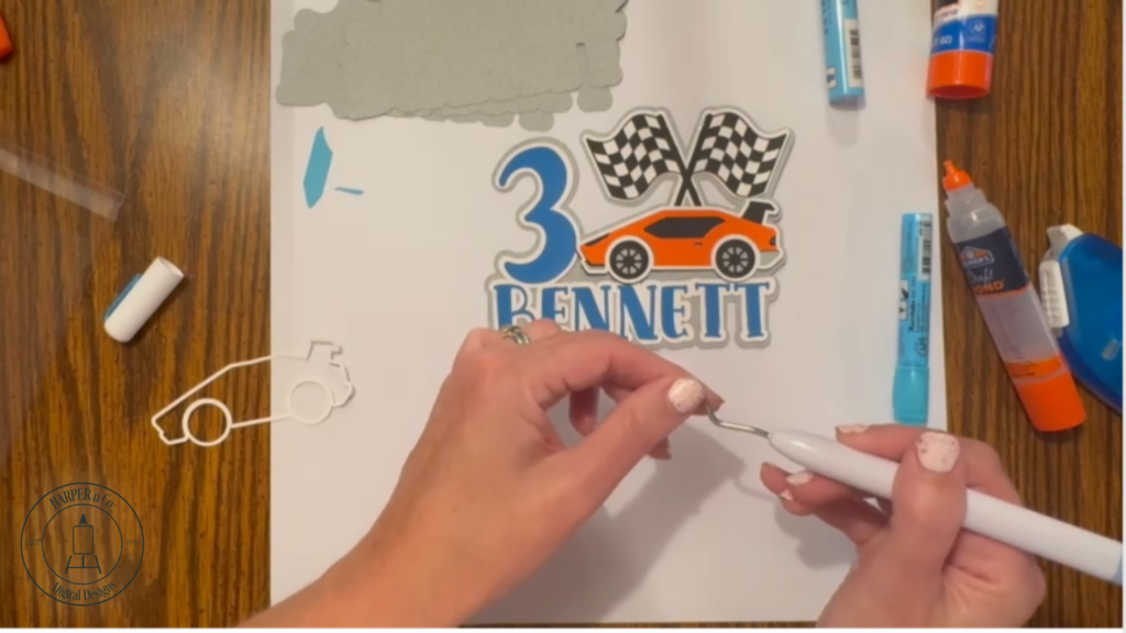Adding orange car body, blue windows, and red tail light to a layered cardstock cake topper.