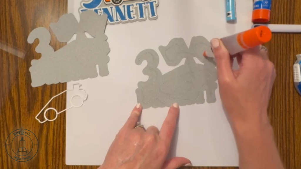 Multiple gray cardstock layers glued together with sticks attached to the back of a custom cake topper for stability.