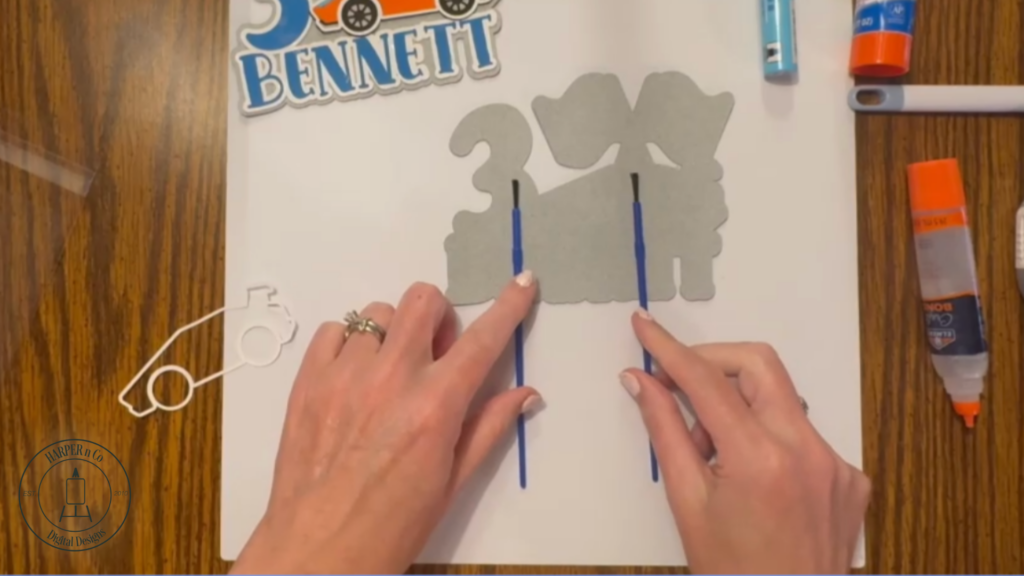 Multiple gray cardstock layers glued together with sticks attached to the back of a custom cake topper for stability.