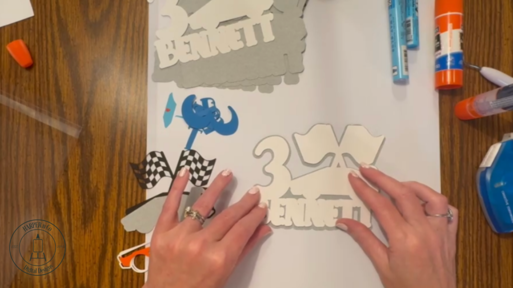 White cardstock layers glued onto a gray base layer to form the foundation of a custom cake topper.